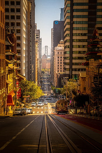 Capture of a bustling San Francisco street featuring a tram, skyscrapers, and the Bay Bridge. HD phone wallpaper