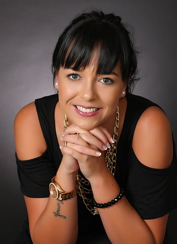 Portrait of an elegant woman smiling, showcasing jewelry and a tattoo against a dark background. HD phone wallpaper