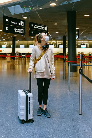 A woman in a face mask stands with her luggage in an empty airport terminal. HD phone wallpaper