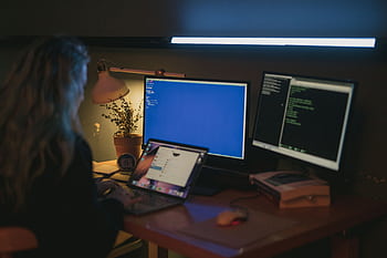 Woman using multiple screens for cybersecurity tasks in a cozy home office HD wallpaper