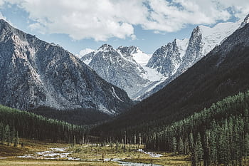 Explore a breathtaking snow-capped mountain range with lush forests and a serene valley during springtime. HD wallpaper