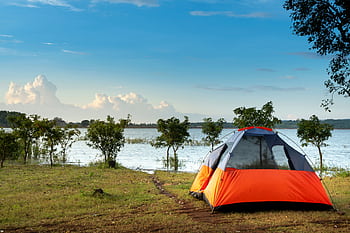 Peaceful lakeside scene with an orange camping tent and clear blue sky. Perfect outdoor adventure. HD wallpaper