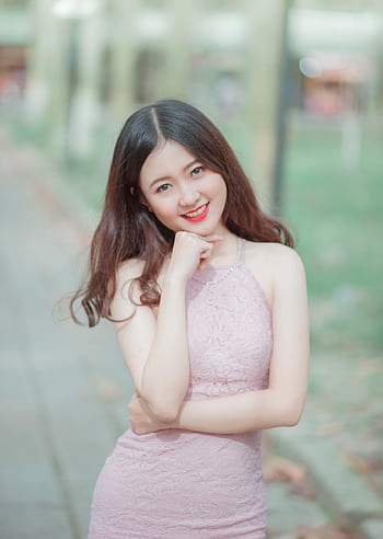 Young woman posing outdoors with a confident smile in an elegant pink dress. HD phone wallpaper