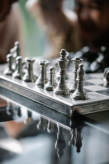 Close-up of metallic chess pieces on a glass table, emphasizing strategic gameplay and elegance. HD phone wallpaper