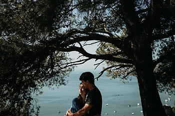 A couple embracing under trees with a scenic ocean view, conveying love and tranquility. HD wallpaper