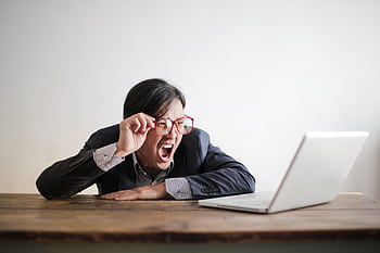 Portrait of a businessman expressing frustration while looking at a laptop in an office setting. HD wallpaper