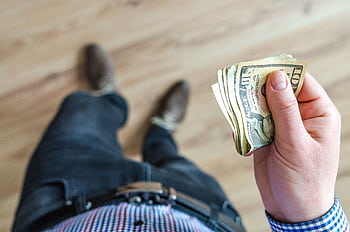 Close-up shot of a man holding US dollar bills indoors with a wooden floor background. HD wallpaper