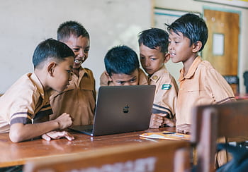 A group of young boys in school uniforms collaborating over a laptop in a classroom setting. HD wallpaper