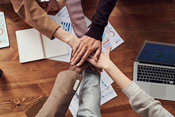 Diverse professionals unite for teamwork around a wooden table with laptops and documents. HD wallpaper