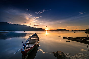 Tranquil sunset view with a boat on a calm lake reflecting mountains and golden sky. HD wallpaper