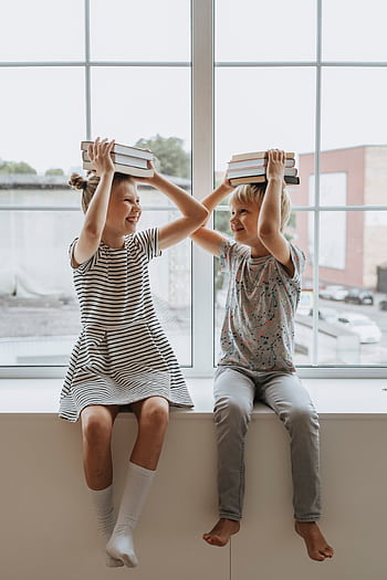 Two happy children playing with books, embodying the joy of learning together. HD phone wallpaper