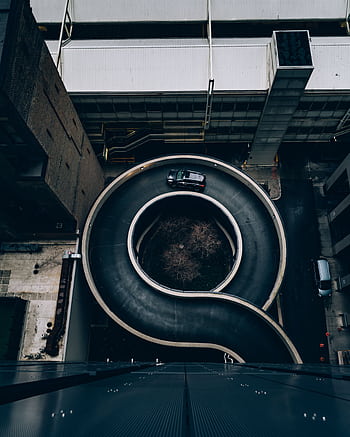 Aerial view of a modern spiral parking ramp in an urban landscape with parked cars. HD phone wallpaper