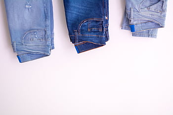 Three pairs of denim jeans neatly folded and hanging against a white backdrop. HD wallpaper