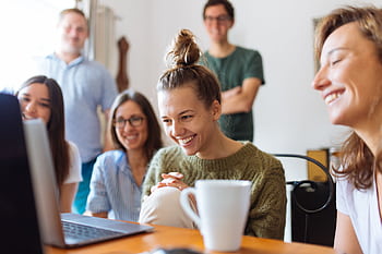 A group of friends enjoying a moment together indoors, smiling and watching a video on a laptop. HD wallpaper