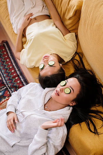 Two women enjoying a relaxing spa day with cucumber masks in a cozy home setting. HD phone wallpaper