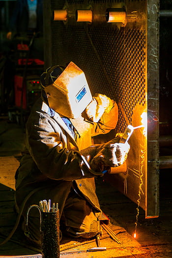 A skilled welder works with a torch in an industrial environment, showcasing metalwork expertise. HD phone wallpaper