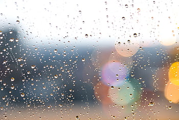 Raindrops on a window with colorful bokeh lights in the background, creating a dreamy atmosphere. HD wallpaper
