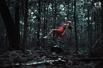 A woman in a red dress appears to levitate in a mysterious forest setting, evoking magic and creativity. HD wallpaper
