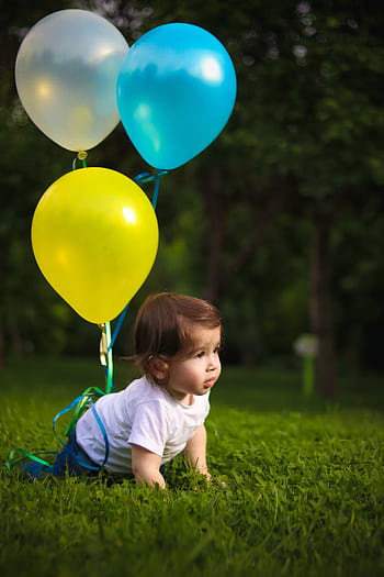 A cute baby crawling on grass with colorful balloons in a lush park setting. HD phone wallpaper