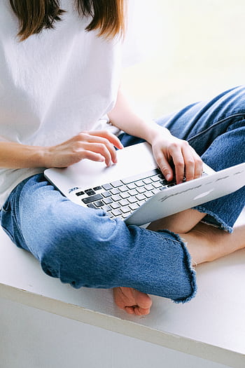 Woman sitting cross-legged in casual jeans working on a laptop indoors. HD phone wallpaper