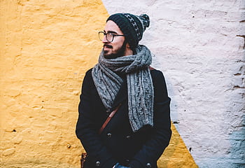 Man in winter attire with scarf and beanie looks away from camera against a vibrant wall. HD wallpaper