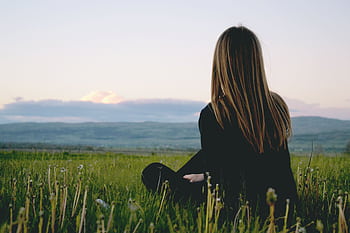 Woman enjoying peace in a lush green field with a scenic mountain view during sunset. HD wallpaper