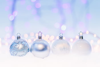 Four snow-covered Christmas ornaments set against a dreamy holiday bokeh backdrop. HD wallpaper
