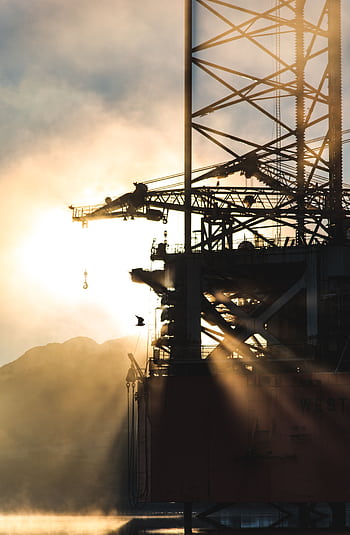 Dramatic silhouette of industrial machinery against a foggy morning sunrise, capturing the essence of heavy industry. HD phone wallpaper