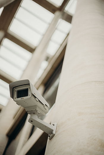 Close-up of a security camera on a building wall, showcasing surveillance technology. HD phone wallpaper