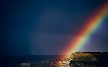 A vibrant rainbow arches over dramatic coastal cliffs during sunset, highlighting nature's beauty. HD wallpaper