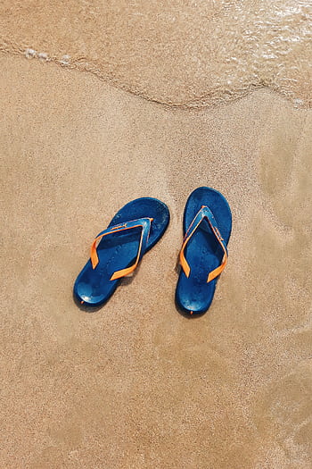 Pair of blue flip flops on golden sand with gentle waves in the background. HD phone wallpaper