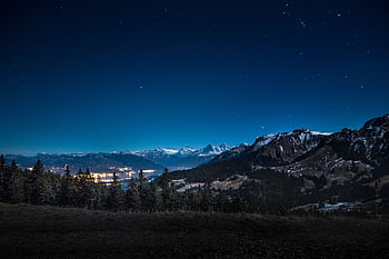 Captivating starry night overlooking illuminated town and mountainous backdrop. HD wallpaper