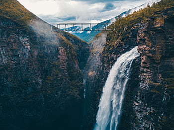 Stunning aerial shot of a waterfall cascading down a rocky gorge with a bridge above in Norway's wilderness. HD wallpaper
