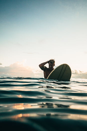 A surfer enjoys the serene waters and a stunning sunset on the coast of Indonesia, perfect for adventurers. HD phone wallpaper