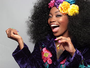A joyful woman with colorful flowers in her afro, exuding happiness and vibrant style. HD wallpaper