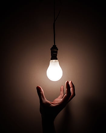 A hand reaching towards a glowing hanging light bulb symbolizing creativity and illumination. HD phone wallpaper