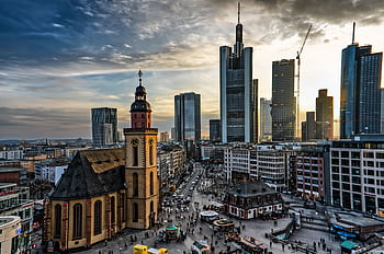 A stunning cityscape of Frankfurt featuring skyscrapers and a historic church at sunset. HD wallpaper