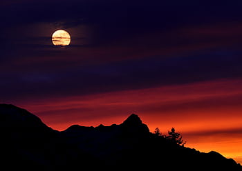 A captivating scene of a full moon above silhouetted mountain peaks against a vivid sunset sky. HD wallpaper