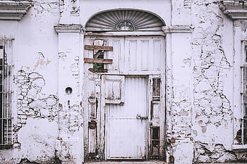 An old, decaying white building with a weathered door and cracked walls. HD wallpaper
