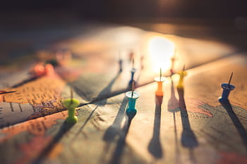 A close-up view of colorful push pins casting shadows on a world map during sunset, highlighting global travel. HD wallpaper