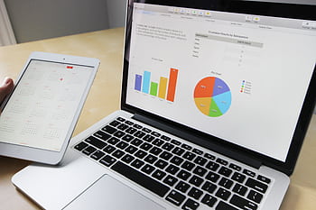 Laptop displaying charts and graphs with tablet calendar for data analysis and planning. HD wallpaper