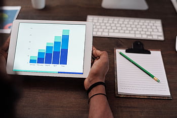 Close-up of a person holding a tablet showing growth charts on a wooden desk setup. HD wallpaper
