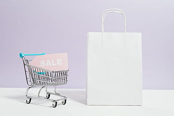 A miniature shopping cart with a sale sign beside a paper bag, perfect for online shopping themes. HD wallpaper