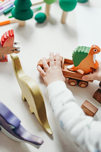 Child's hands interact with vibrant wooden toy dinosaur set, creating playful scene on tabletop. HD phone wallpaper