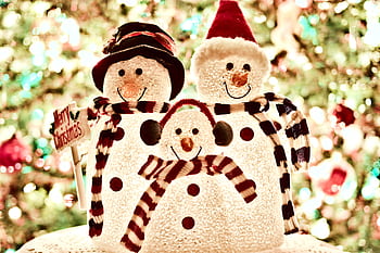 Close-up of a cheerful snowman family decoration with bright Christmas lights in the background. HD wallpaper