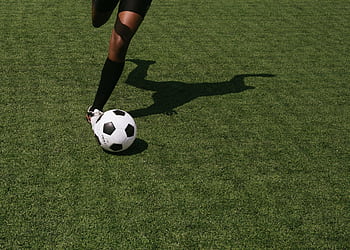 Cropped shot of a soccer player in motion, performing a kick on a grassy sports field under daylight. HD wallpaper
