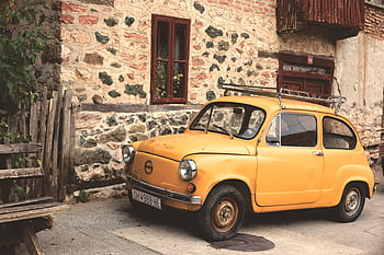 Old yellow car parked by a rustic stone building embracing vintage charm. HD wallpaper