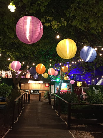 Vibrant paper lanterns hanging over a garden path during a festive night celebration outdoors. HD phone wallpaper