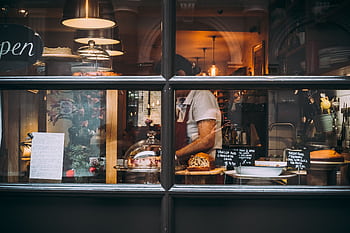Warm bakery scene in London through window showcasing pastries and chef at work. HD wallpaper