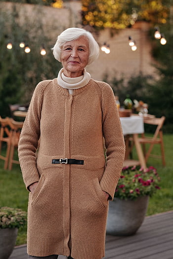 Cheerful senior woman in a cozy cardigan enjoying an outdoor gathering in the garden. HD phone wallpaper